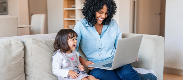 A woman and young girl laugh on the couch while looking at a laptop.